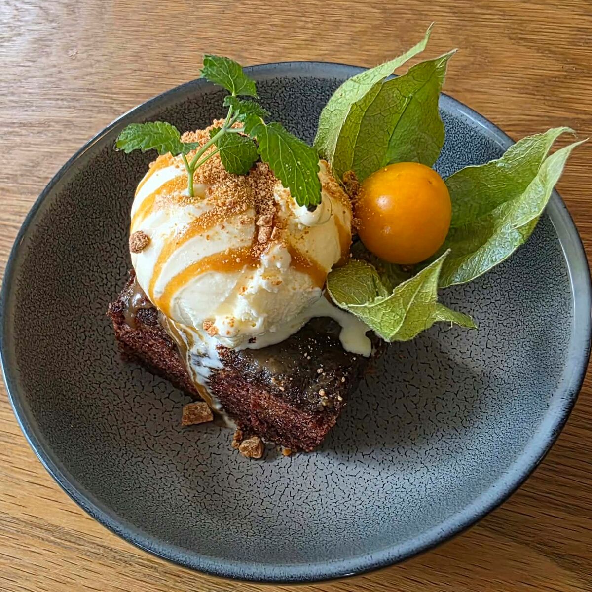 Sticky toffee pudding med vaniljeis, karamellsaus, smuler, mynte og en fysalis